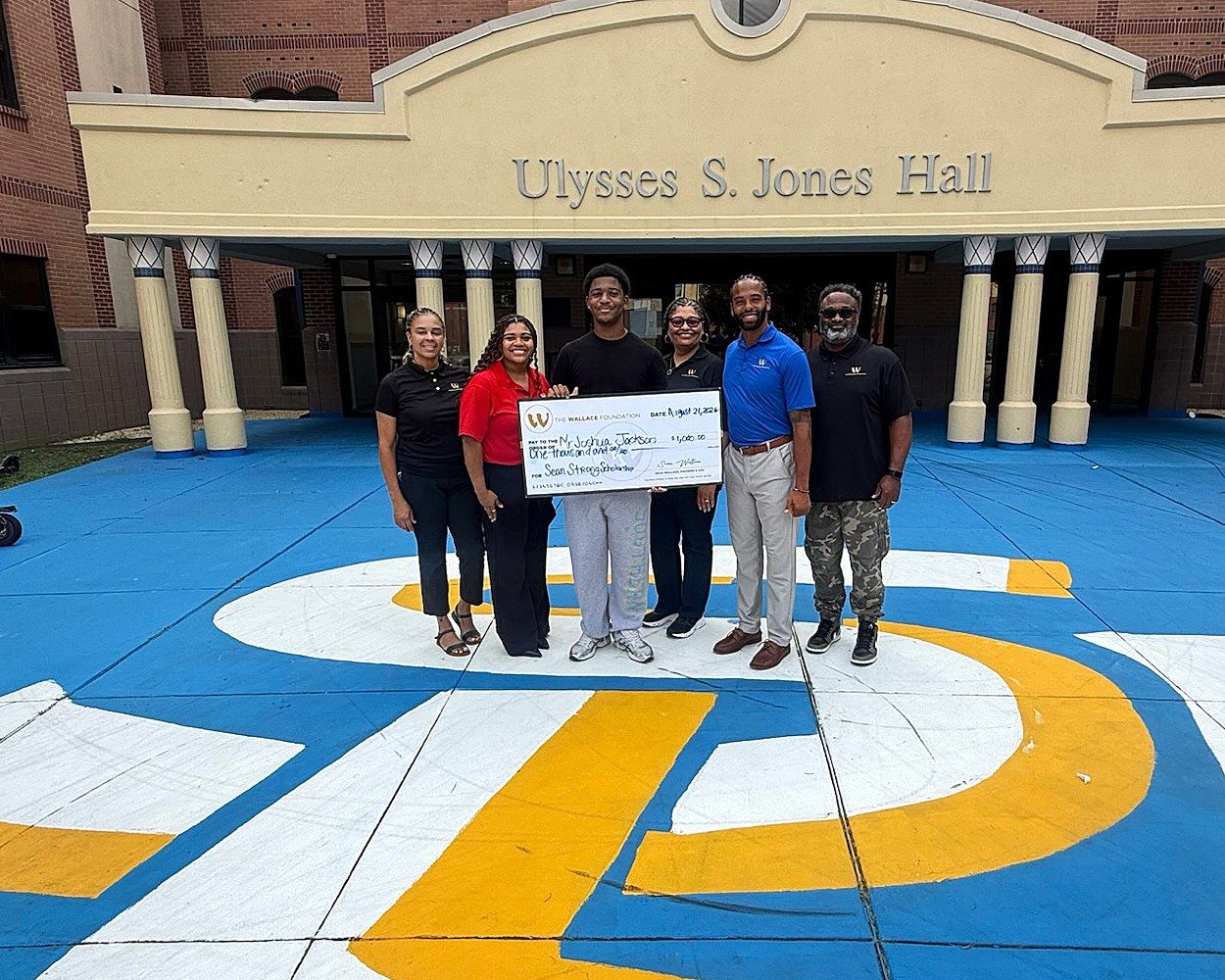 Six people outside Ulysses S. Jones Hall holding an oversized Wallace Foundation cheque presented for the Sean Strong Scholarship.